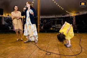 A flower girl playfully leans upside down and peeks at her yellow dress during toasts at a wedding in Blue Hill, Maine.